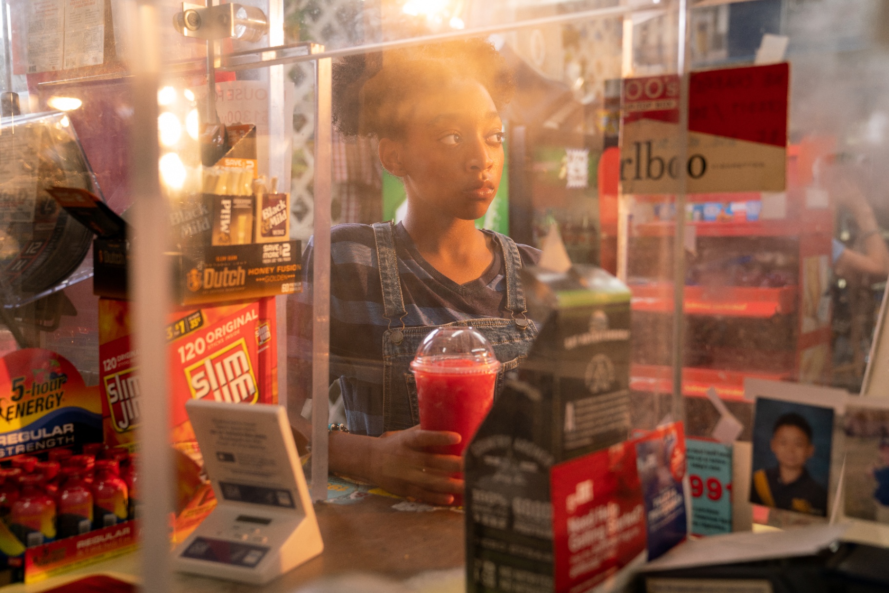 Cherry Lemonade — interior still of the lead behind a lemonade stand counter, mid-conversation with a customer